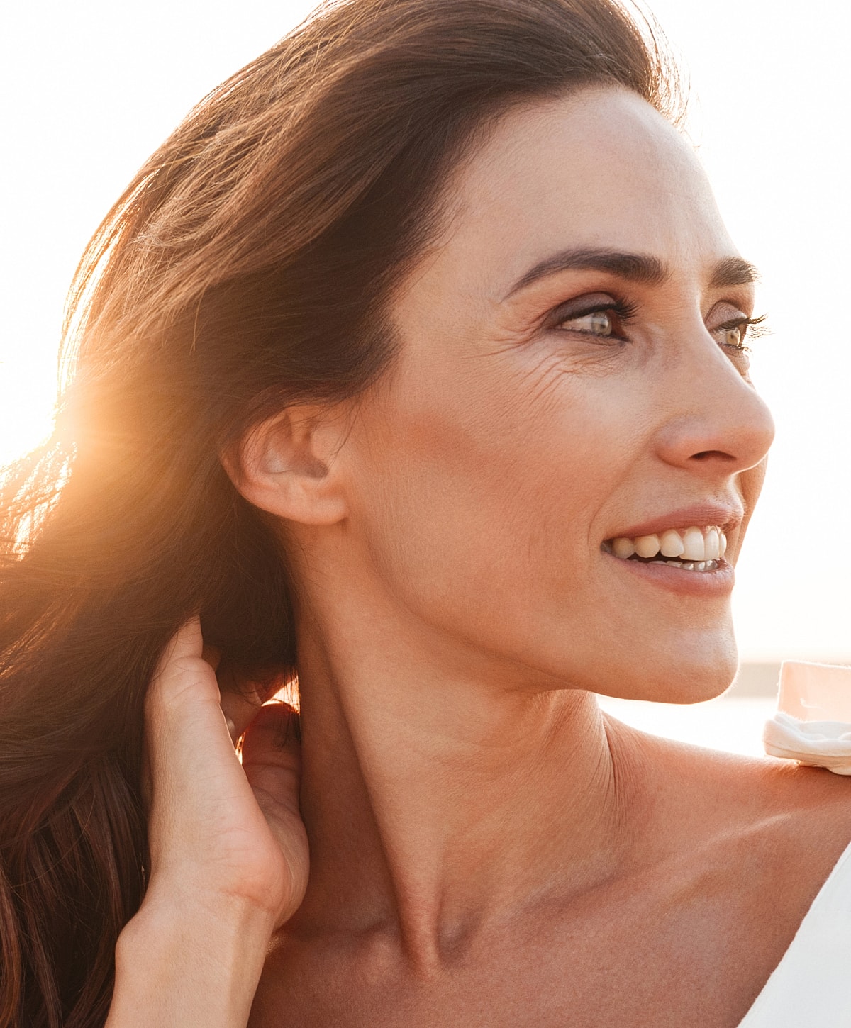 Smiling woman outdoors with sunlight backdrop.