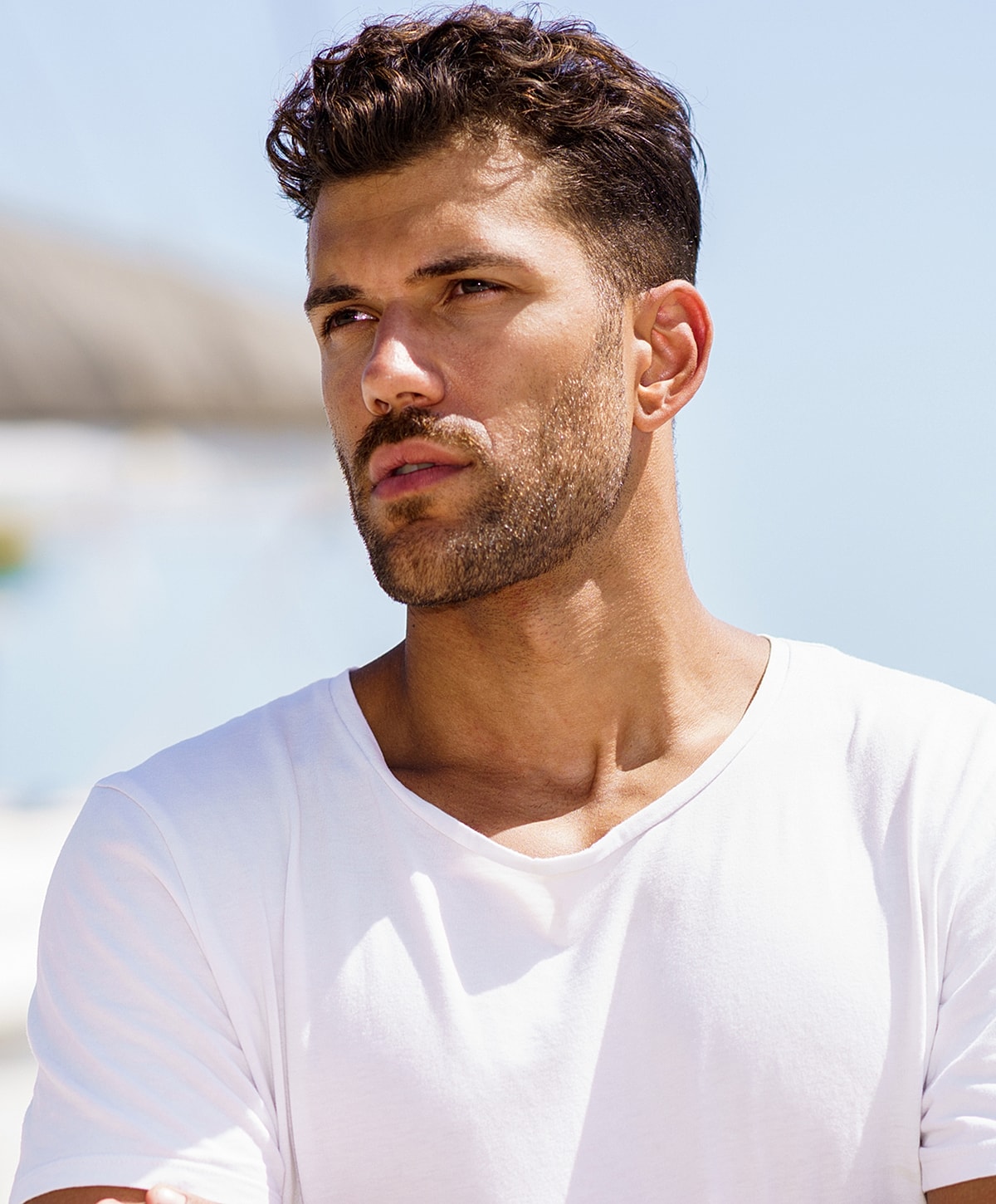 Young man in white shirt outdoors, thoughtful expression.