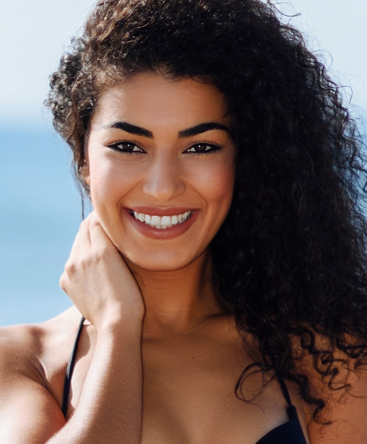 Smiling woman with curly hair by the beach.