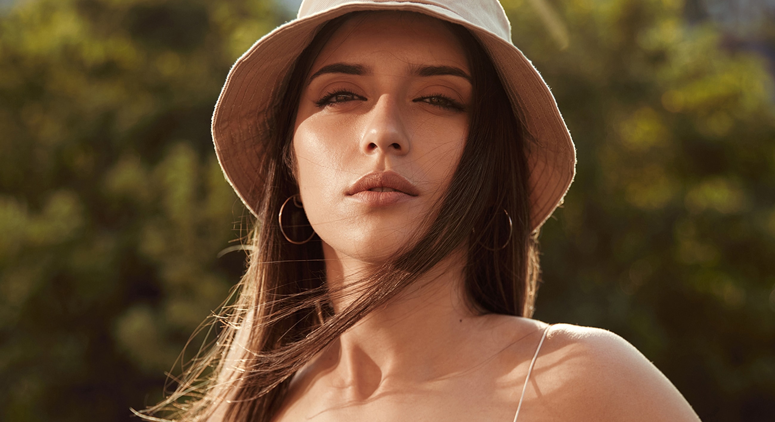 Woman with hat outdoors, sunlight, and gentle breeze.